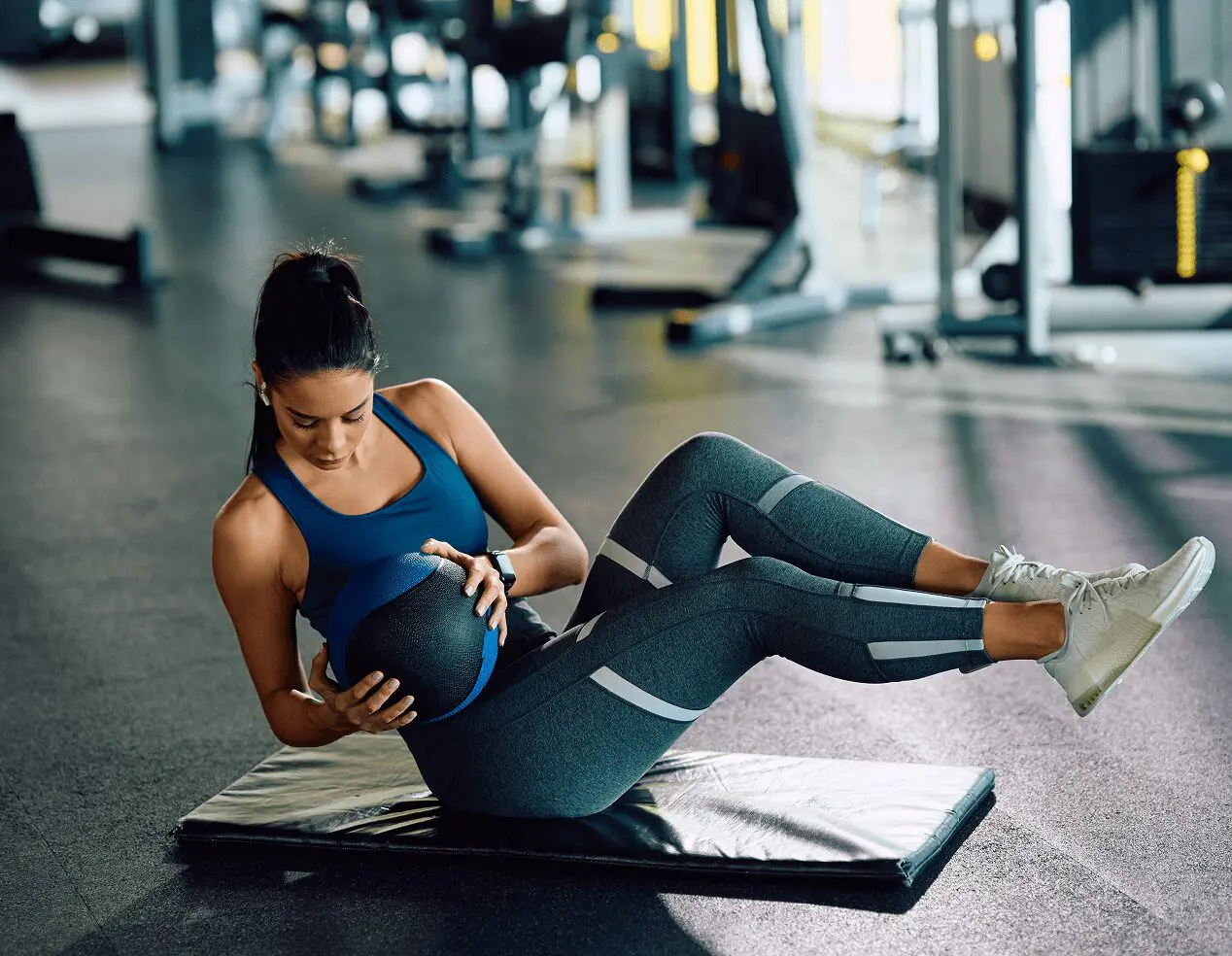 A woman in athletic wear exercises on a mat at home, performing a twisting motion while holding a medicine ball, part of her invigorating in-home personal training routine.